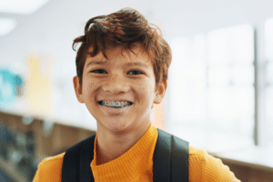 Smiling young boy wearing metal braces and a backpack.